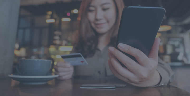 A woman in a coffee shop holding her phone and credit card.