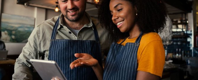 Smiling male and female colleagues looking at tablet.