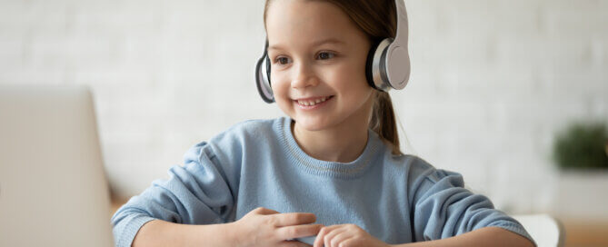Little schoolgirl learning school subject distantly using pc and headphones.
