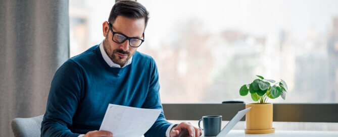 Young adult businessman sitting at desk looking at papers.