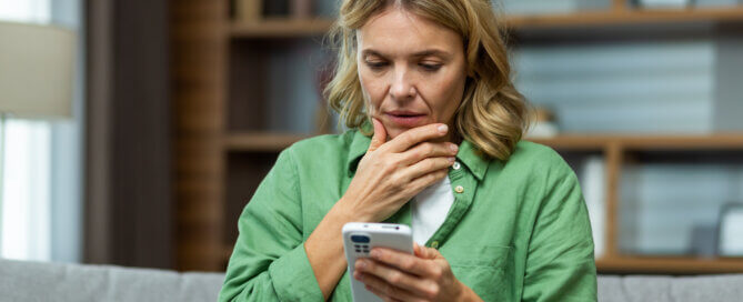 Worried woman sitting on sofa at home holding phone.